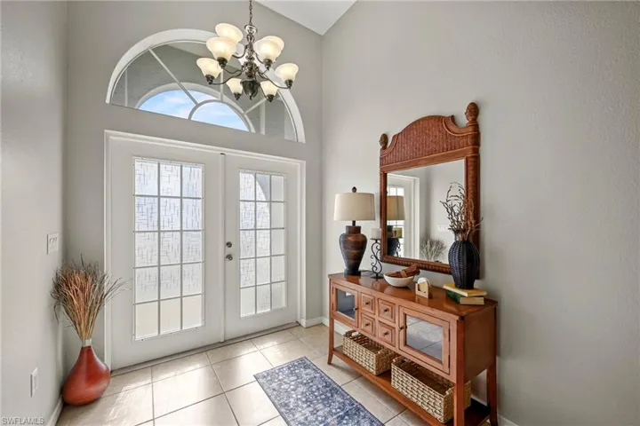 Entrance foyer with a chandelier, french doors, lofted ceiling, and light tile patterned floors