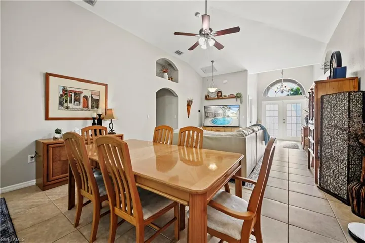 Dining space featuring french doors, arched walkways, vaulted ceiling, a ceiling fan, and light tile patterned flooring