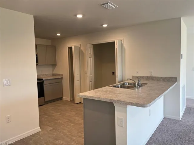 Kitchen with a peninsula, gray cabinets, a kitchen bar, stainless steel range oven, and light countertops