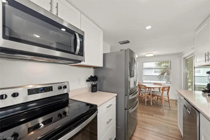 Kitchen featuring stainless steel appliances, white cabinets, light wood-style flooring, recessed lighting, and light stone countertops