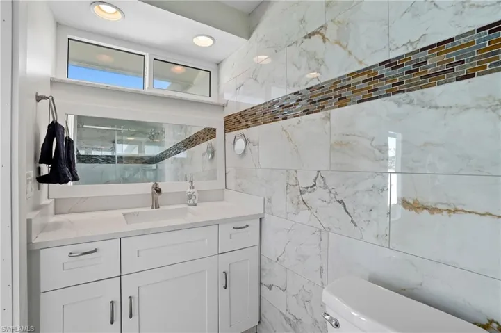 Bathroom with vanity, a marble finish shower, and tile walls - Virtually Edited Image