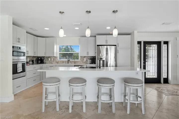 Kitchen featuring decorative light fixtures, backsplash, a kitchen breakfast bar, and recessed lighting - Virtually Edited Image