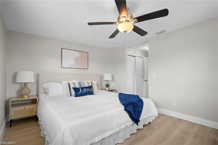 Bedroom featuring wood-finish flooring, a ceiling fan with integrated lighting, a built-in closet with bi-fold doors, and neutral wall tones