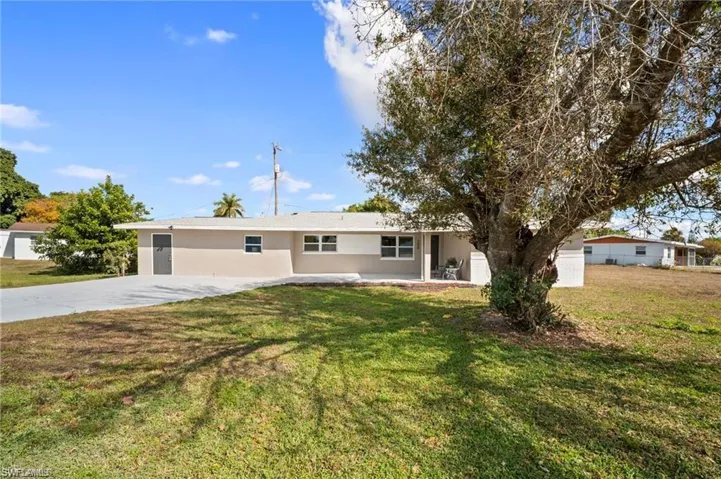 Single-story residence featuring a neutral two-tone exterior, a concrete driveway, and a spacious front yard with mature trees