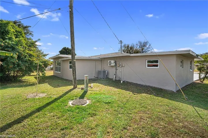 Rear exterior featuring a stucco finish, multiple windows, an air conditioning unit, and a flat roofline