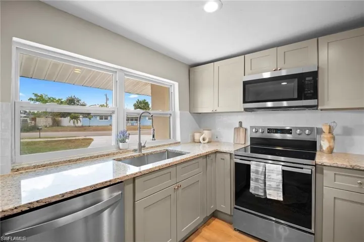 Kitchen featuring a stainless steel undermount sink, granite countertops, updated cabinetry, a tile backsplash, and stainless steel appliances