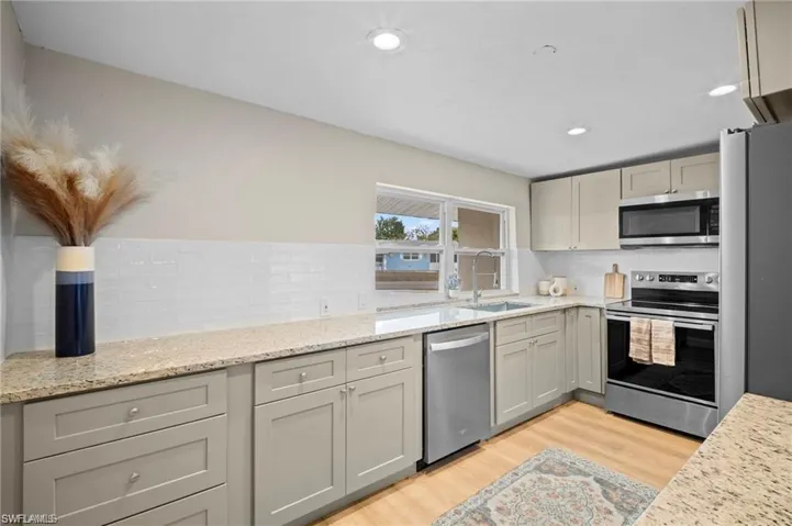 Kitchen featuring light wood-finish flooring, light-toned cabinetry, light-colored countertops, a white subway tile backsplash, and stainless steel appliances