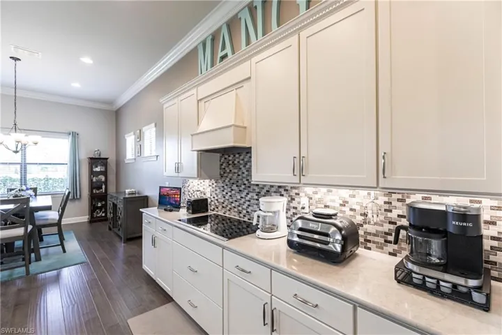 Kitchen featuring black electric stovetop, dark hardwood / wood-style floors, white cabinets, an inviting chandelier, and ornamental molding