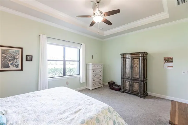 Bedroom with ceiling fan, a tray ceiling, light carpet, and ornamental molding