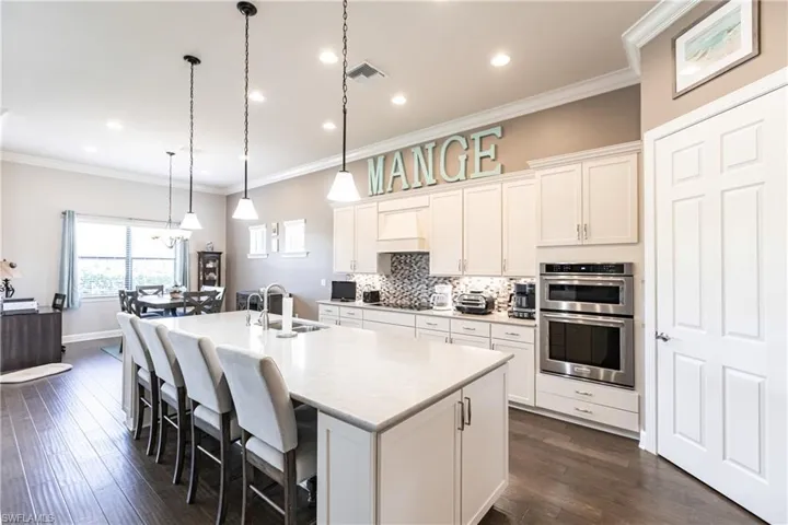 Kitchen featuring white cabinetry, dark wood-type flooring, an island with sink, double oven, and sink