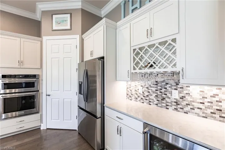 Kitchen featuring appliances with stainless steel finishes, ornamental molding, dark wood-type flooring, and white cabinets