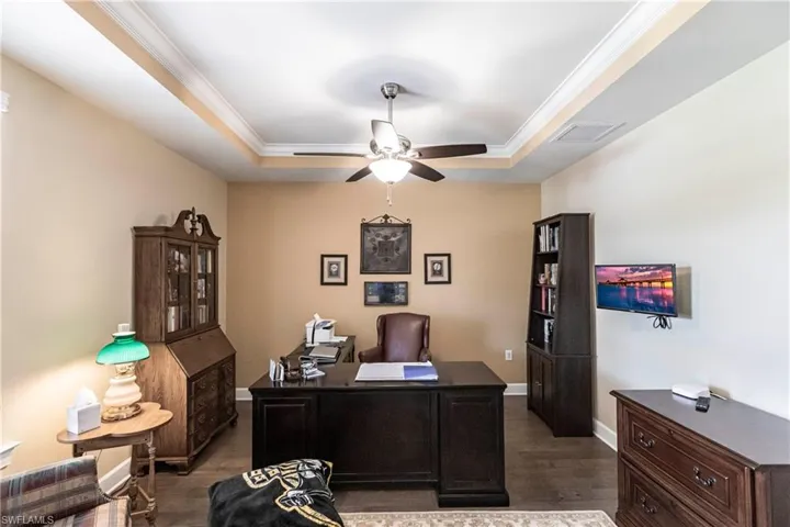 Office area with ceiling fan, a tray ceiling, crown molding, and dark wood-type flooring