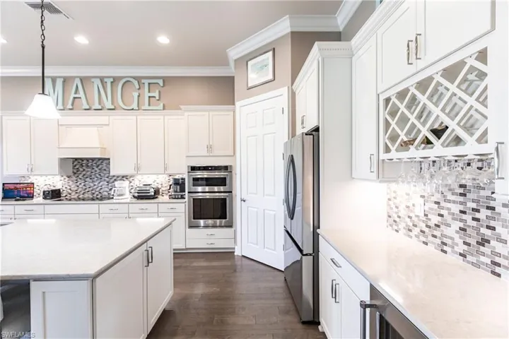 Kitchen with custom exhaust hood, decorative light fixtures, backsplash, stainless steel appliances, and crown molding