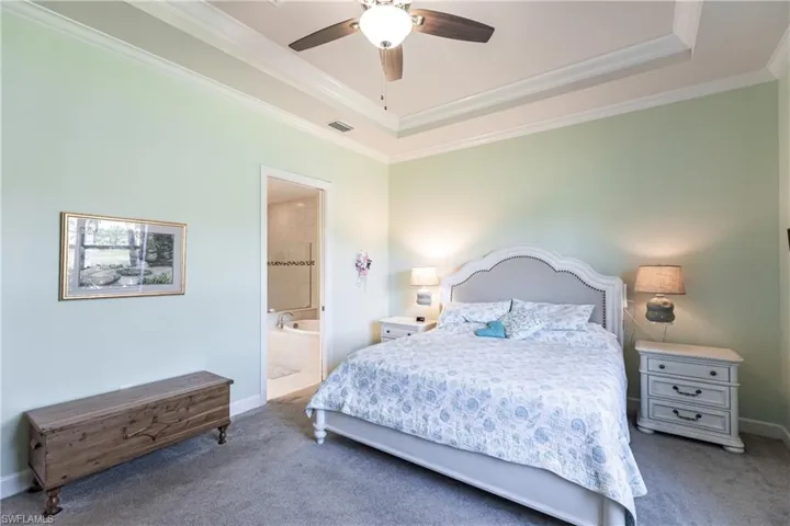 Bedroom featuring a tray ceiling, carpet floors, ensuite bathroom, crown molding, and ceiling fan
