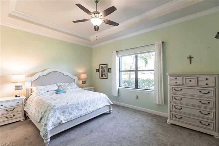 Bedroom with a raised ceiling, carpet, crown molding, and ceiling fan