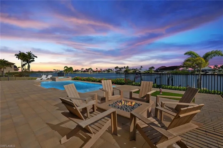 Patio terrace at dusk with a patio, a fire pit, a pool with connected hot tub, and a water view