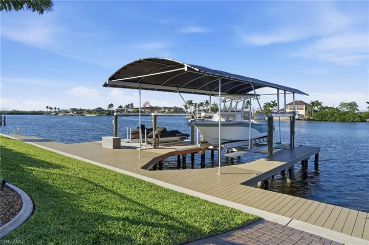 Dock featuring boat lift, a water view, and a yard