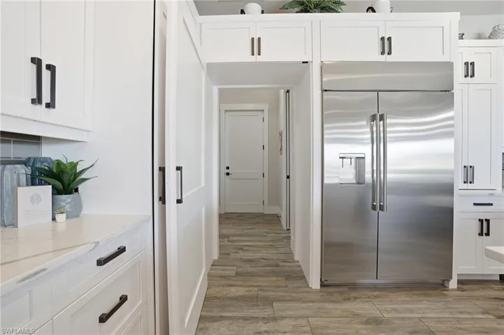 Kitchen with white custom cabinets, stainless steel built in refrigerator and hidden door way
