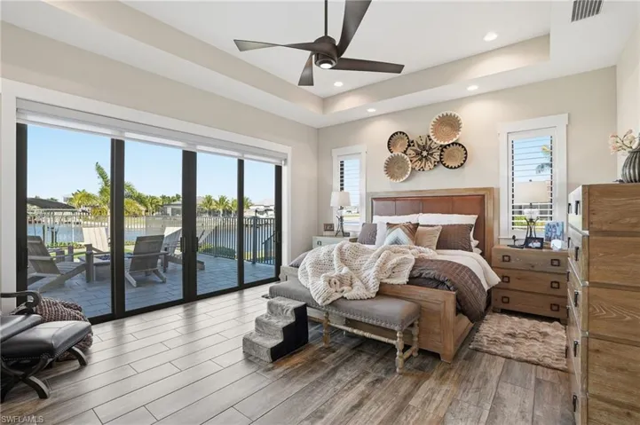 Primary Bedroom with a water view, a raised ceiling, access to exterior, wood finish floors, and recessed lighting