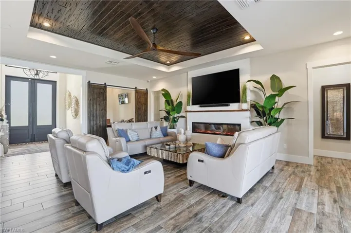 Living area with a raised ceiling, wooden ceiling, a barn door leading to study, light wood-style floors, and electric fireplace