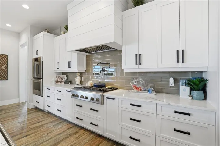 Kitchen featuring white cabinets, premium range hood, light stone counters, light wood-style flooring, and stainless steel appliances
