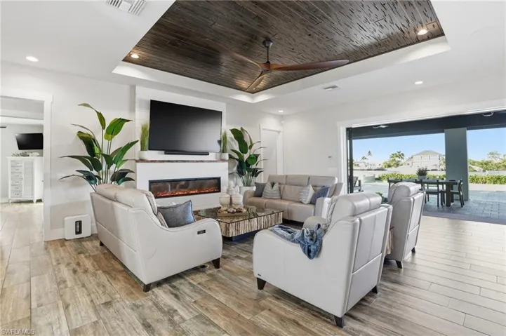 Living area with a raised ceiling, wooden ceiling, light wood finished floors, a glass covered fireplace, and recessed lighting