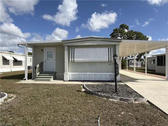 Rear view of house featuring concrete driveway, an attached carport, entry steps, and a lawn