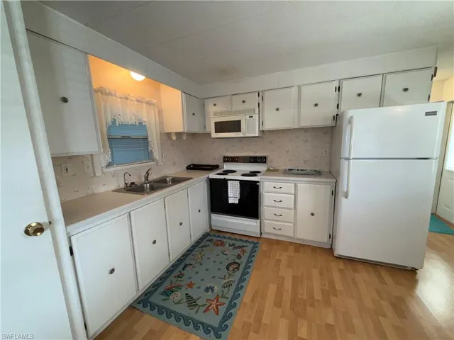 Kitchen featuring white cabinets, white appliances, light countertops, and light wood-style flooring