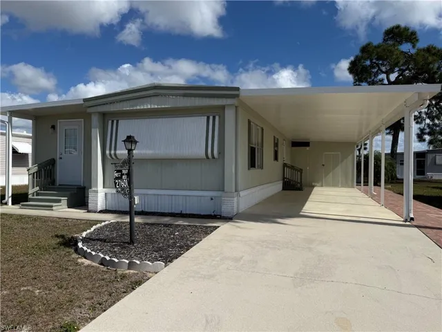 View of front of property featuring concrete driveway, entry steps, a carport, and a front yard