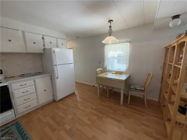 Kitchen with white cabinetry, light countertops, freestanding refrigerator, range, and light wood-type flooring