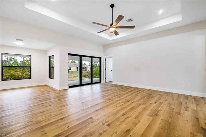 Empty room with ceiling fan, light wood finished floors, and a tray ceiling
