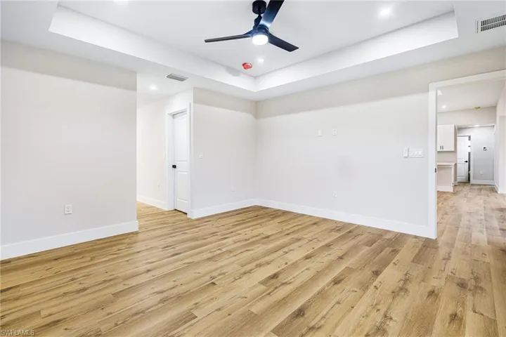 Empty room with a raised ceiling, light wood-type flooring, recessed lighting, and a ceiling fan