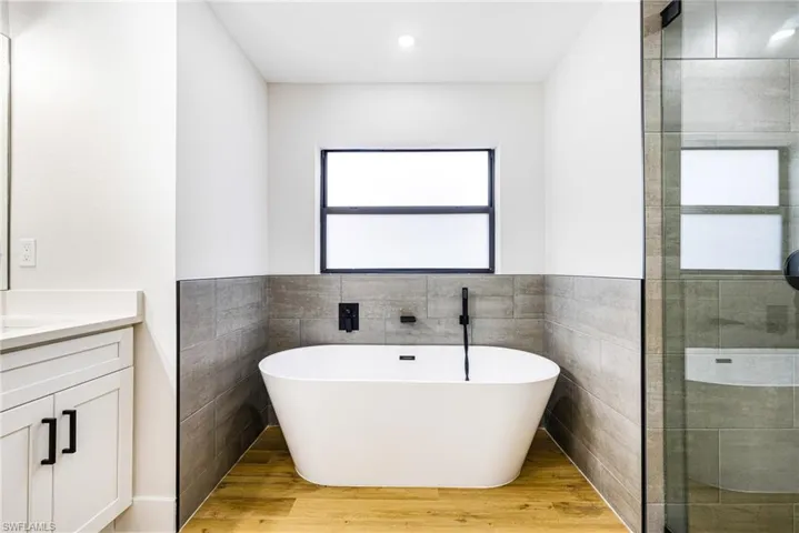 Full bathroom featuring tile walls, a freestanding bath, light wood finished floors, vanity, and a wainscoted wall