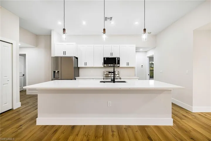 Kitchen with hanging light fixtures, an island with sink, white cabinets, appliances with stainless steel finishes, and light stone counters