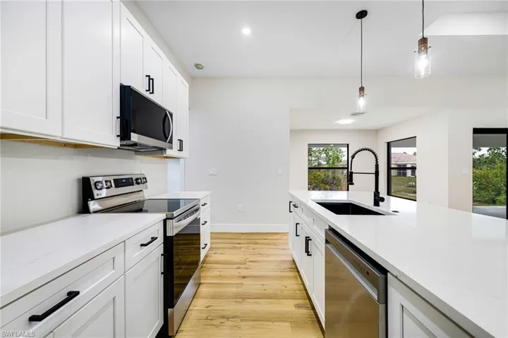 Kitchen with stainless steel appliances, decorative light fixtures, white cabinets, light wood finished floors, and light stone countertops