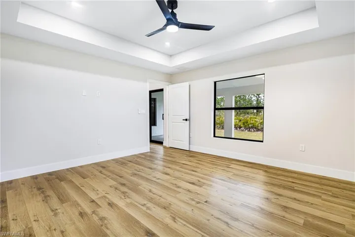 Unfurnished bedroom featuring a raised ceiling, light wood-style floors, a ceiling fan, and recessed lighting