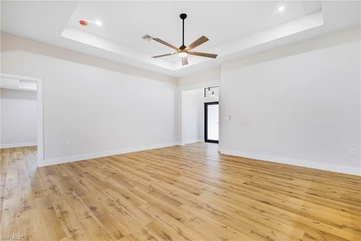 Unfurnished room with light wood-style flooring, ceiling fan, and a tray ceiling