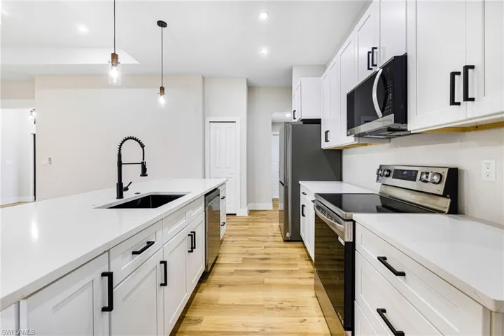 Kitchen featuring appliances with stainless steel finishes, decorative light fixtures, white cabinets, light wood-style flooring, and light stone counters