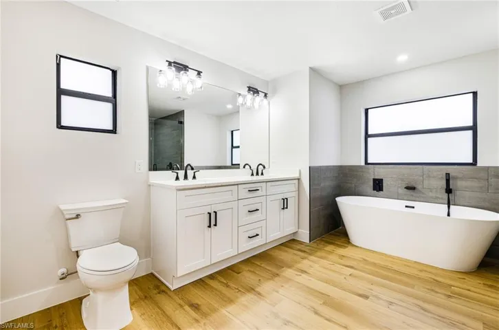 Bathroom with a freestanding tub, double vanity, tile walls, light wood-style floors, and a shower stall