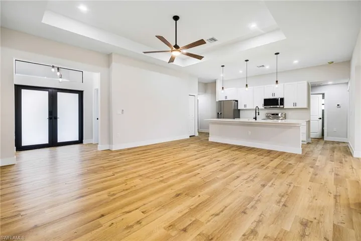 Unfurnished living room featuring light wood-style flooring, a raised ceiling, a ceiling fan, and recessed lighting