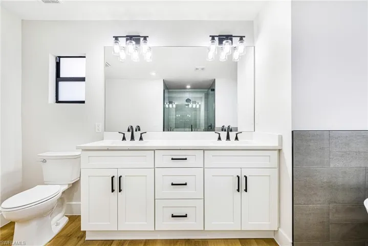 Full bath featuring a shower stall, double vanity, and light wood finished floors