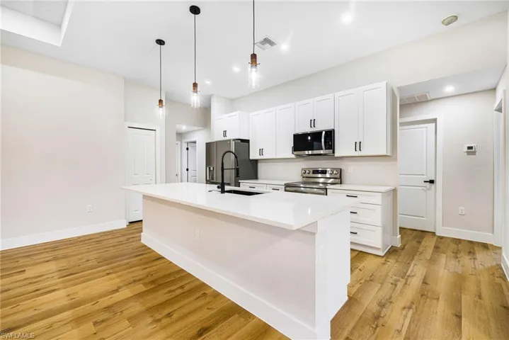 Kitchen featuring white cabinets, decorative light fixtures, appliances with stainless steel finishes, an island with sink, and light wood finished floors