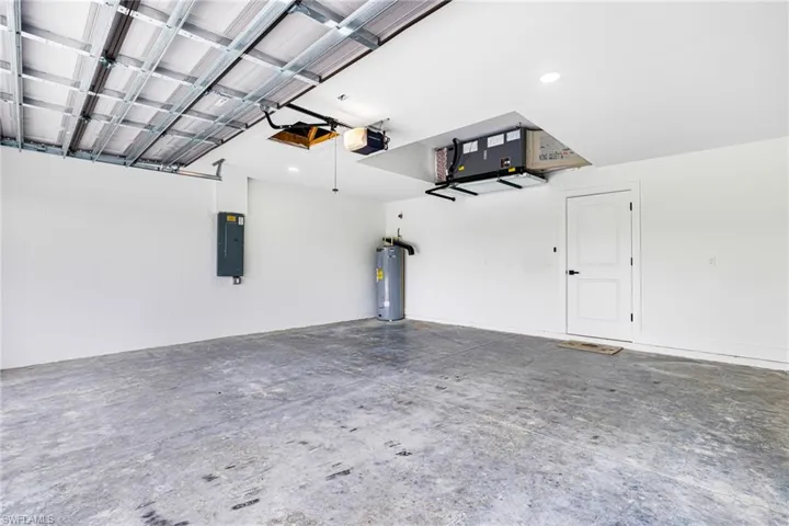 Garage with electric panel, electric water heater, and a garage door opener
