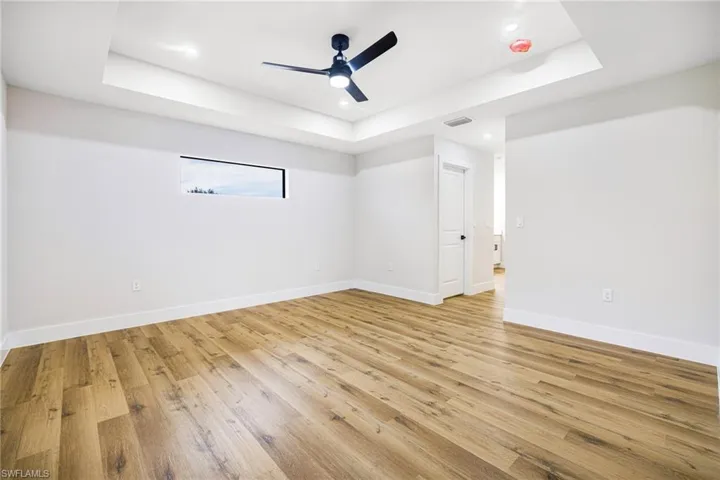 Empty room with light wood-style floors, a ceiling fan, a tray ceiling, and recessed lighting