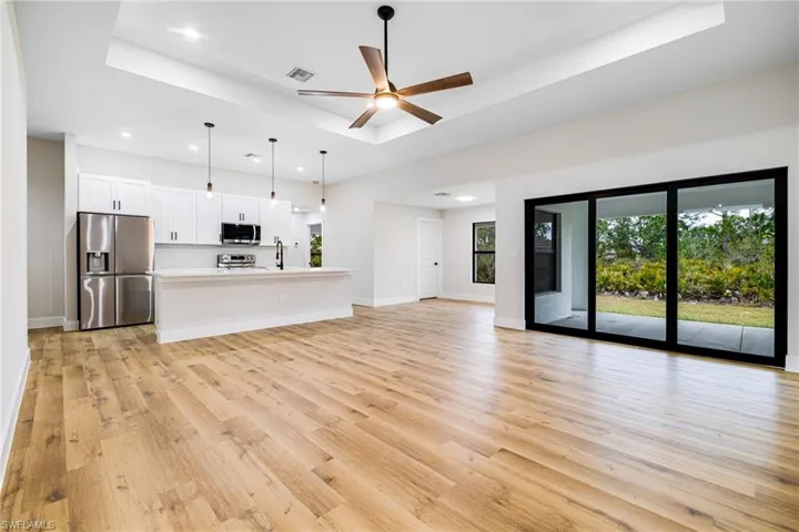 Unfurnished living room with a tray ceiling, a ceiling fan, light wood-style flooring, and recessed lighting