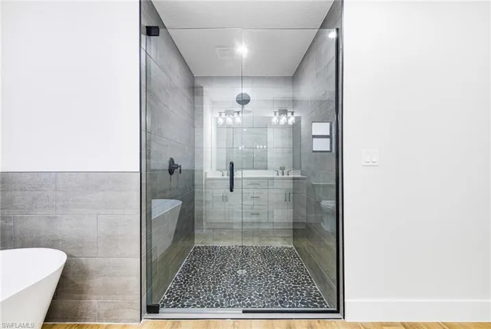 Bathroom featuring a freestanding bath, a stall shower, wood finished floors, and tile walls