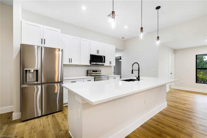 Kitchen featuring appliances with stainless steel finishes, pendant lighting, white cabinetry, a center island with sink, and recessed lighting