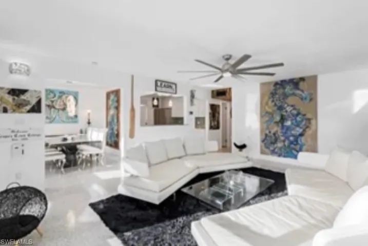 Bright living area featuring light-toned flooring, a modern ceiling fan, and a pass-through opening to an additional room