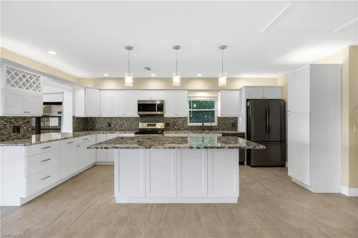 Kitchen with appliances with stainless steel finishes, white cabinets, light tile patterned floors, and backsplash