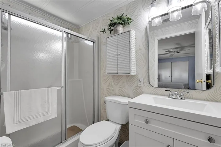 Bathroom featuring wallpapered walls, a stall shower, vanity, a ceiling fan, and crown molding